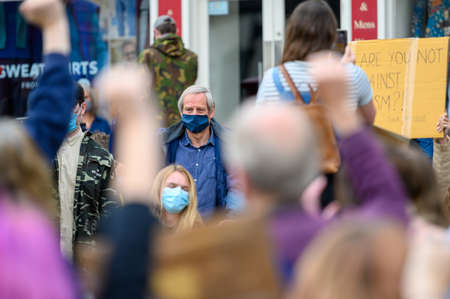 Richmond, North Yorkshire, UK - June 14, 2020: An elderly gentleman protester wears a PPE face mask at a Black Lives Matter protest in Richmond, North Yorkshire. Out of focus protesters raised hands in salute in the foreground.のeditorial素材