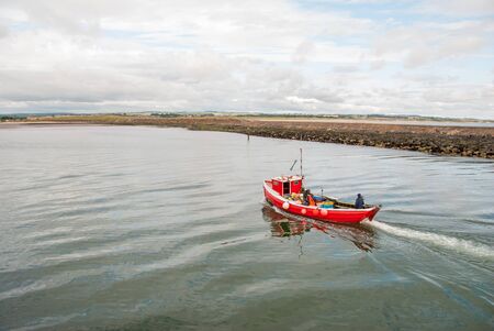 A small red fishing boat on a calm day.