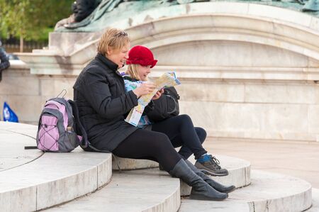 Mother and young daughter tourists sit on old stone steps and check a map.の写真素材