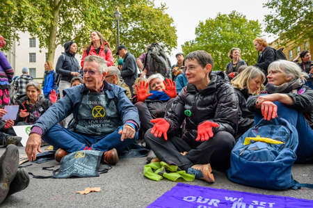 LONDON - OCTOBER 18, 2019: Mature Extinction Rebellion Protesters with red painted hands sat on a roadのeditorial素材
