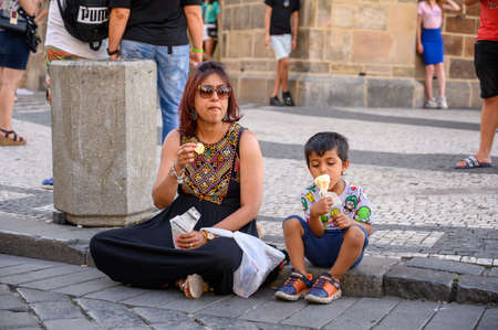 PRAGUE - JULY 20, 2019: A mother and her son sat on a curbside eating snacksのeditorial素材