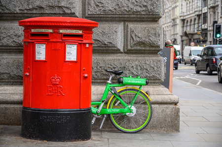 LONDON - FEBRUARY 04, 2020: A Lime electric assist rental bike parked between a wall and a traditional red British Post Boxのeditorial素材
