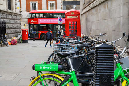 LONDON - FEBRUARY 04, 2020: A Lime electric assist rental bike parked with regular bicycles with a Red London Double Decker Bus, a traditional red phone box and post box in the backgroundのeditorial素材