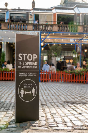 LONDON - SEPTEMBER 12, 2020: Covid 19 Social Distancing warning sign at Covent Garden with diners at an outdoor restaurant in the backgroundのeditorial素材
