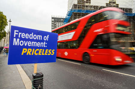 Red London Double Decker bus with motion blur passes anti-Brexit Freedom of Movement sign outside...