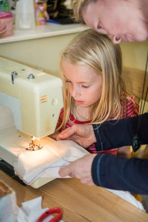 Close up of a mother teaching young daughter to use a sewing machine.の写真素材
