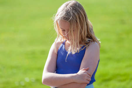 Moody young blonde girl with arms folded sulks in a field.の写真素材