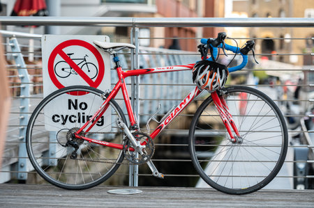 London, UK - November 2, 2020: Red bike leaning against a No Cycling sign on metal railings.