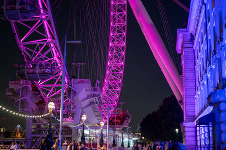 LONDON - SEPTEMBER 14, 2021: Illuminated London Eye next to County Hall with people passing by at nightのeditorial素材