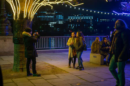 LONDON - NOVEMBER 5, 2021: Shoppers pose for a photograph beneath the Southbank Christmas decorations at nightのeditorial素材