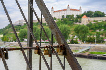 BRATISLAVA, SLOVAKIA - JULY 9, 2019: Rusty old padlocks on Most SNP bridge with Bratislava Castle out of focus in the backgroundのeditorial素材