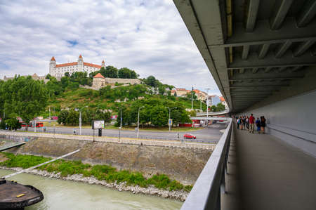BRATISLAVA, SLOVAKIA - JULY 9, 2019: Tourists crossing the Most SNP bridge with Bratislava Castle in the backgroundのeditorial素材