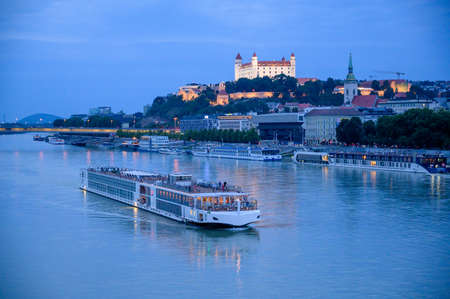 BRATISLAVA, SLOVAKIA - JULY 9, 2019: A river cruise boat passes along the River Danube in front of Bratislava Castle in the blue light of eveningのeditorial素材