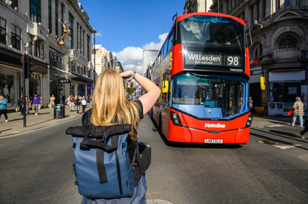 LONDON - May 18, 2022: Blonde female photographer taking photograph of red Double Decker Bus on busy London Streetのeditorial素材