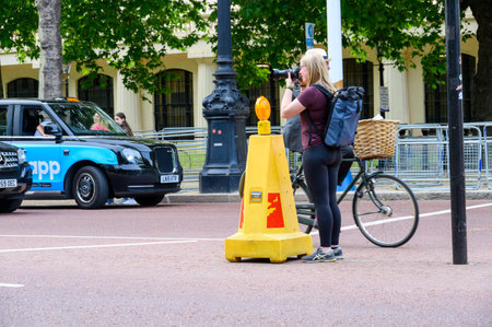 LONDON - May 18, 2022: Blonde female photographer with backpack takes photograph in middle of the...