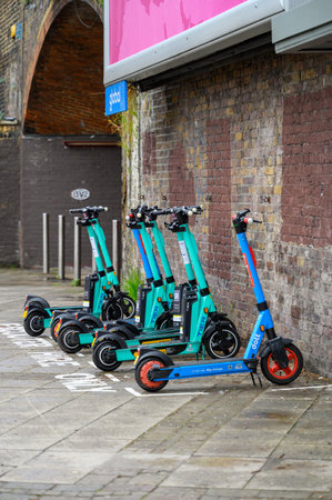 LONDON - May 20, 2022: Electric Rental Scooters lined up on pavement next to old brick wall