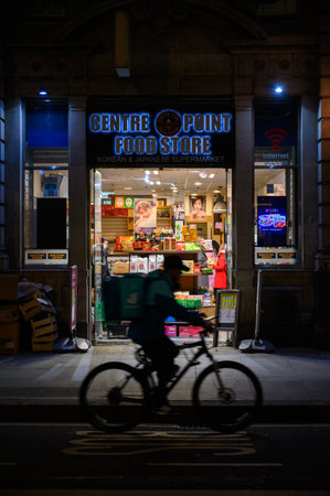 LONDON - November 3, 2020: Centre Point Food Store entrance at night with motion blurred silhouette of delivery cyclist in passing in frontのeditorial素材