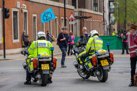 LONDON - April 22, 2023: Metropolitan police officers on motorcycles maintain order and ensure public safety at the Extinction Rebellion protest in London, while a protester passes, waving a flag.のeditorial素材