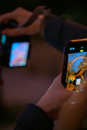 LONDON - April 22, 2023: Capture the moment: A hand holds a mobile phone, framing orange lights on...