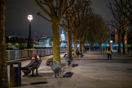 LONDON - April 22, 2023: Serene Southbank night scene with people, trees, benches. St Paul's Cathedral shines in background.のeditorial素材
