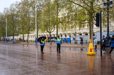 LONDON - April 24, 2023: Stewards in reflective jackets work on a rainy day, directing pedestrians...