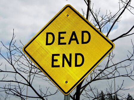 A dead end sign with a defoliated tree in the background lends an ominous toneの写真素材