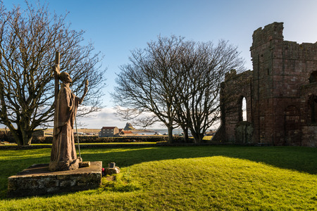 St Aidan Statue - Statue of St Aidan the founder of the Lindisfarne Monastery overlooks the ruins todayの写真素材
