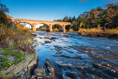Bywell Bridge crosses River Tyne, as it flows through Northumberland, under the stone arched Bywell Road Bridge near Stocksfieldの写真素材