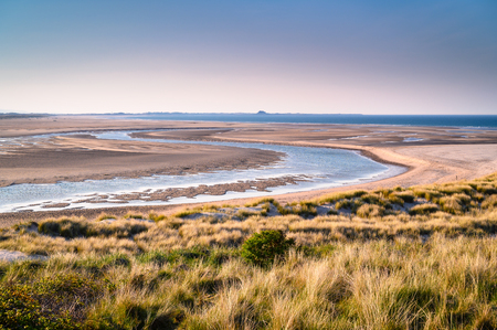 Budle Water meanders to the North Sea, the mud flats at Budle Bay at low tide are part of Lindisfarne Nature reserve on Northumberland's AONB coastlineの写真素材