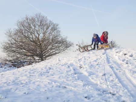 boy and girl in winter clothing with wooden sledges at the top of a snow covered duneの写真素材