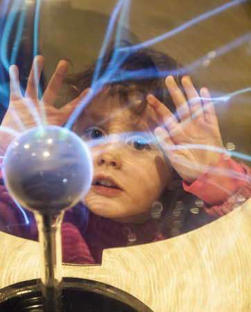 small girl touches a plasma ball with her hands and watches the electrostatic dischargeの写真素材
