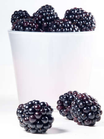 fresh blackberries on a white cutting board with a white glass full of blackberries in the backgroundの写真素材