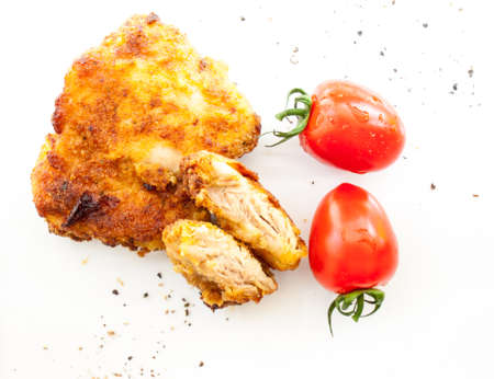 sliced fried breaded chicken with red plum tomatoes and black peper on a whiet backgroundの写真素材