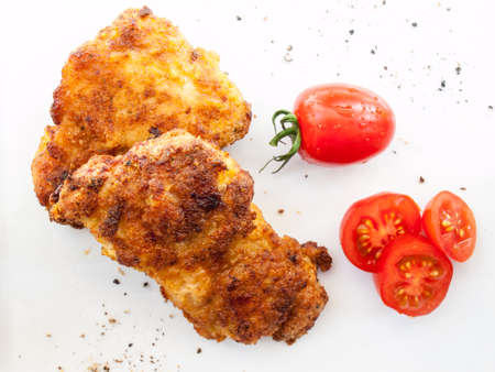 fried breaded chicken with sliced red plum tomatoes and black peper on a whiet backgroundの写真素材