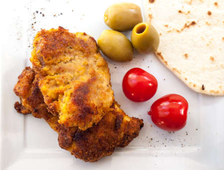 fried breaded chicken  red cherry tomatoes  green olives and  a flat bread wrap on a white plateの写真素材