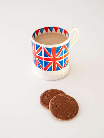 A cup of milky english tea in a british union jack mug with chocolate digestive biscuitsの写真素材