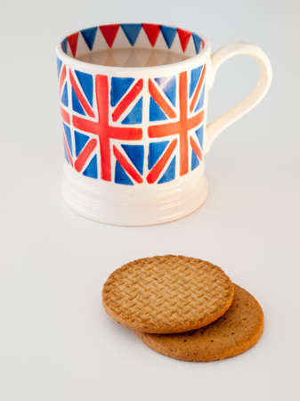 A cup of milky english tea in a british union jack mug with  digestive biscuitsの写真素材