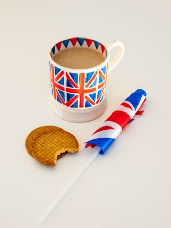 A cup of milky english tea in a british union jack mug with  digestive biscuits and a british flagの写真素材