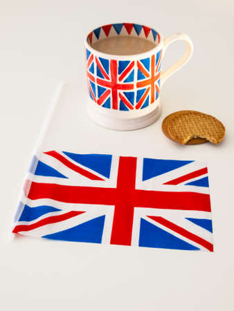 A cup of milky english tea in a british union jack mug with  digestive biscuits and a british flagの写真素材