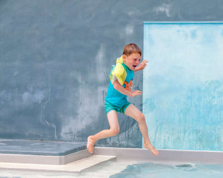 small boy in armbands jumping into an outdoor swimming poolの写真素材