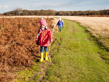 Small boy and small girl in winter cloths, woolen hats and rubber boots walking in a sunny winter dune landscape の写真素材