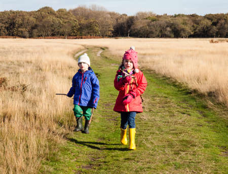 Small boy and small girl in winter cloths, woolen hats and rubber boots walking in a sunny winter dune landscape の写真素材