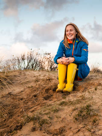 portrait of middle aged woman  in winter clothing and rubber boots in  a sunny autumn dune landscapeの写真素材