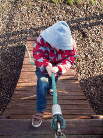 small boy in winter clothing climbing up a rope in an outdoor adventure playgroundの写真素材