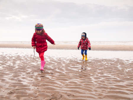 small boy and girl in winter clothing and rubber boots spalshing in a tidal pool on a winter beachの写真素材