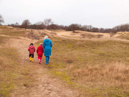 woman with small boy and girl in winter clothing and rubber boots on a winter day walking through a dune landscapeの写真素材