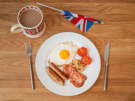 English breakfast on a wooden table with cup of tea  and british flag in landscapeの写真素材