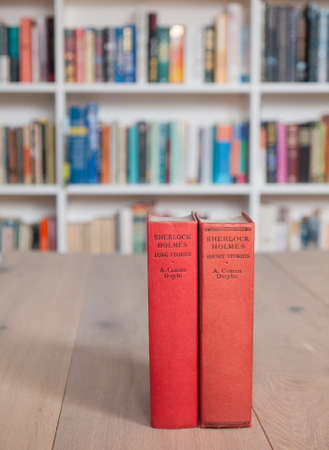 Aged copies of sherlock holmes long and short stories standing on a wooden table with a book shelf full of books in soft focus behindのeditorial素材