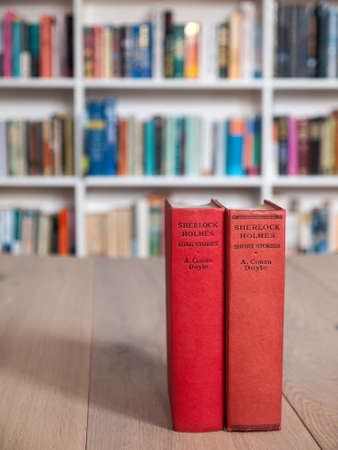 Aged copies of sherlock holmes long and short stories standing on a wooden table with a book shelf full of books in soft focus behindのeditorial素材