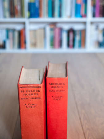 Aged copies of sherlock holmes long and short stories standing on a wooden table with a book shelf full of books in soft focus behindのeditorial素材